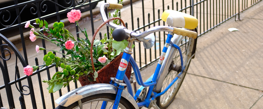 A retro blue bike next to a fence with pink flowers in its basket