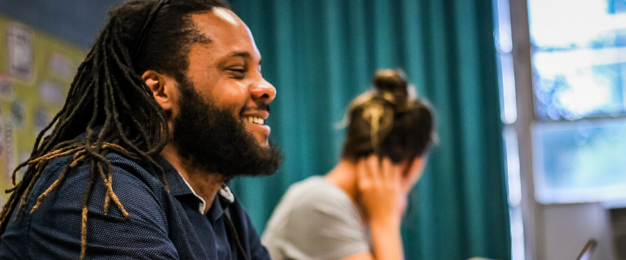 An African American man with dreadlocks smiles in a group meeting.