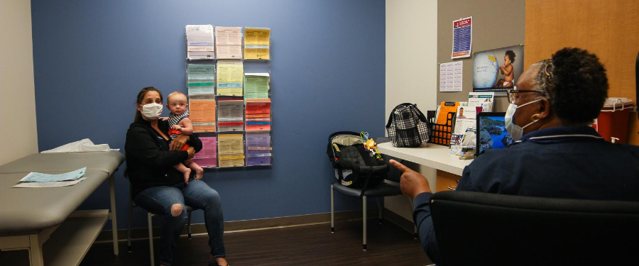 A masked staff member prepares a mom for her baby's vaccine