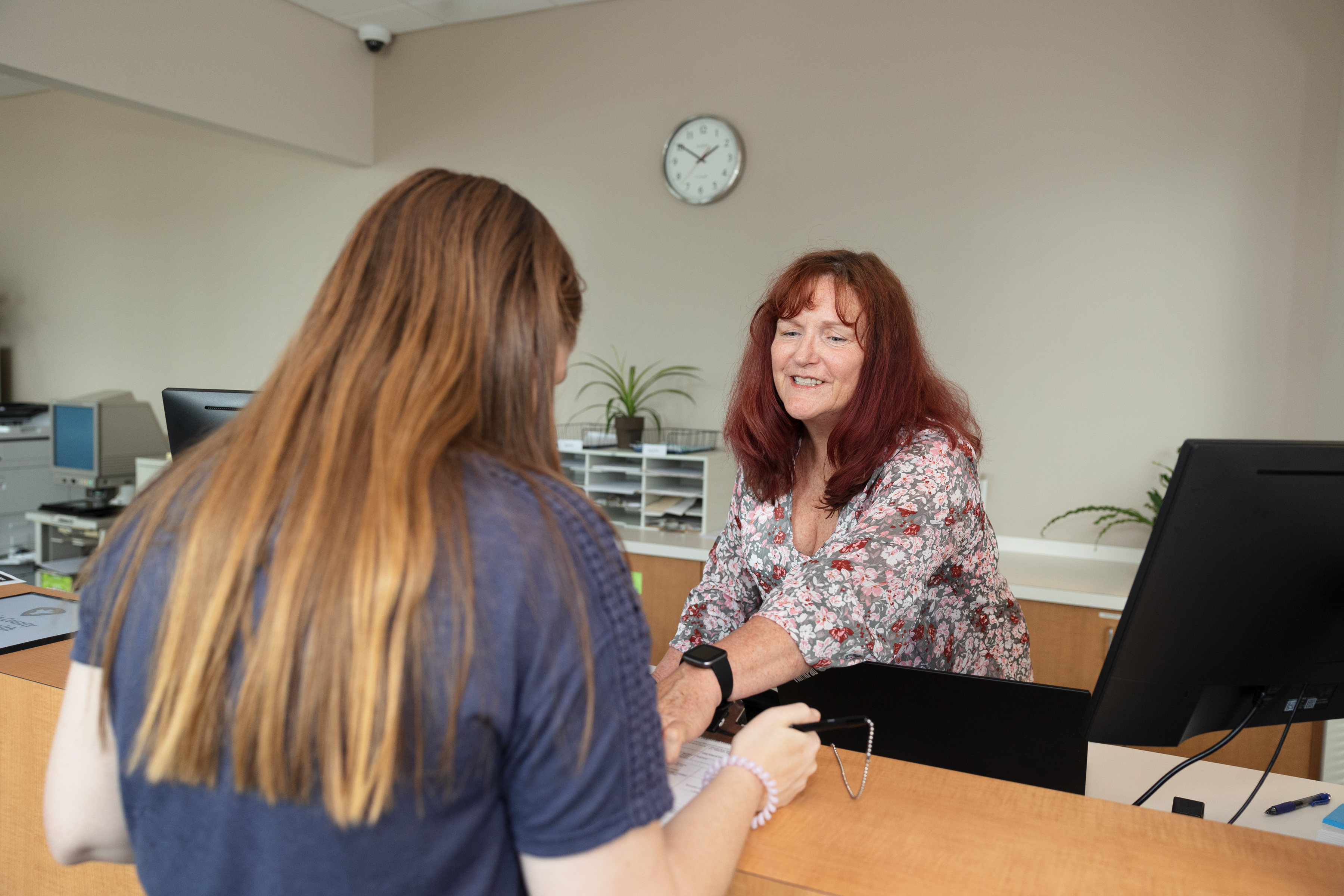 Smiling woman greets customer at the vital statistics counter.