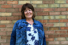 White woman in jean jacket standing in front of a brick wall