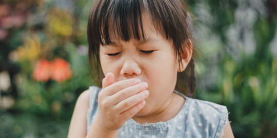 young child coughing with hand covering mouth