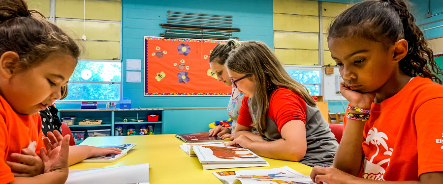 Young students of different races read at a desk.