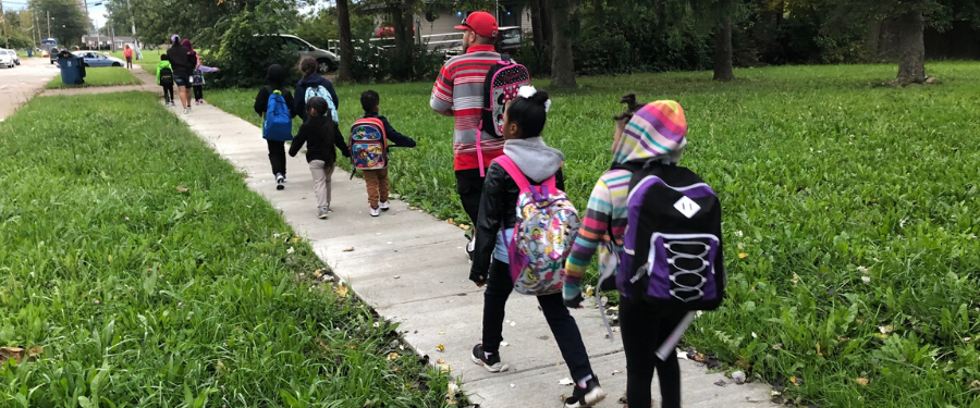 Students walk to school on a sidewalk with an adult.