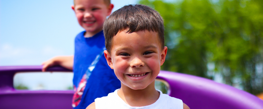 Two boys smile at the camera while they play on a playground.