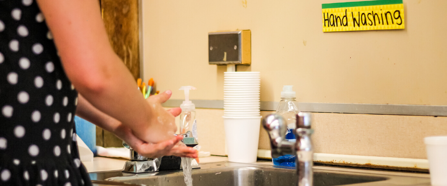 A young girl at a school sink washing her hands