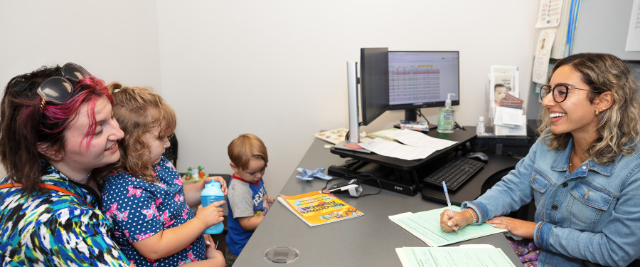 A woman smiling while filling out paperwork with a client and her children 